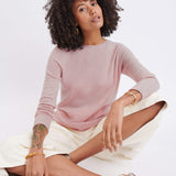 female wearing light pink sweater sitting with legs criss crossed on the floor on white background 