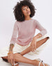 female wearing light pink sweater sitting with legs criss crossed on the floor on white background 