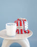 6.5 oz OUI! sandbag candle in light blue and red striped bag on a blue background
