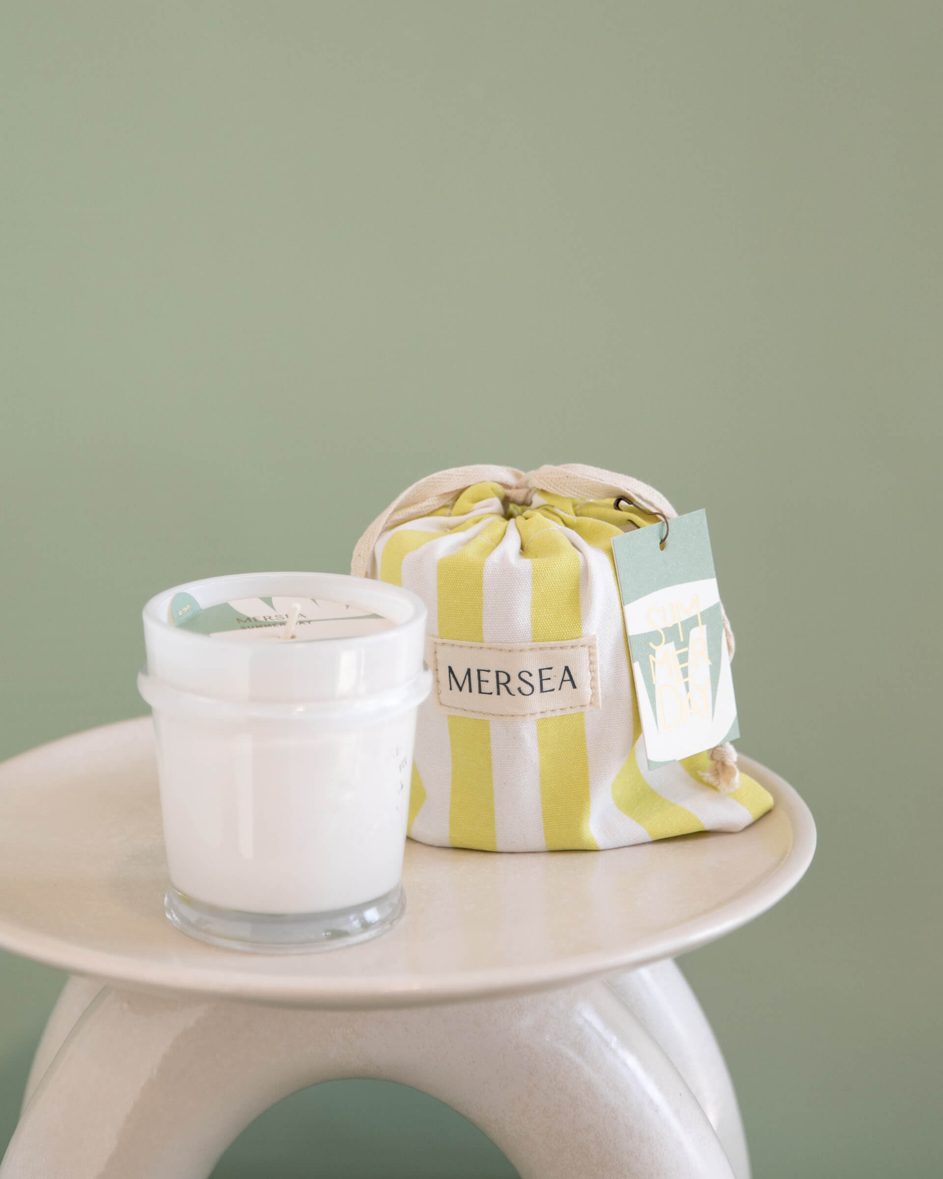 6.5 oz summer day sandbag candle in yellow and white striped bag on a green background
