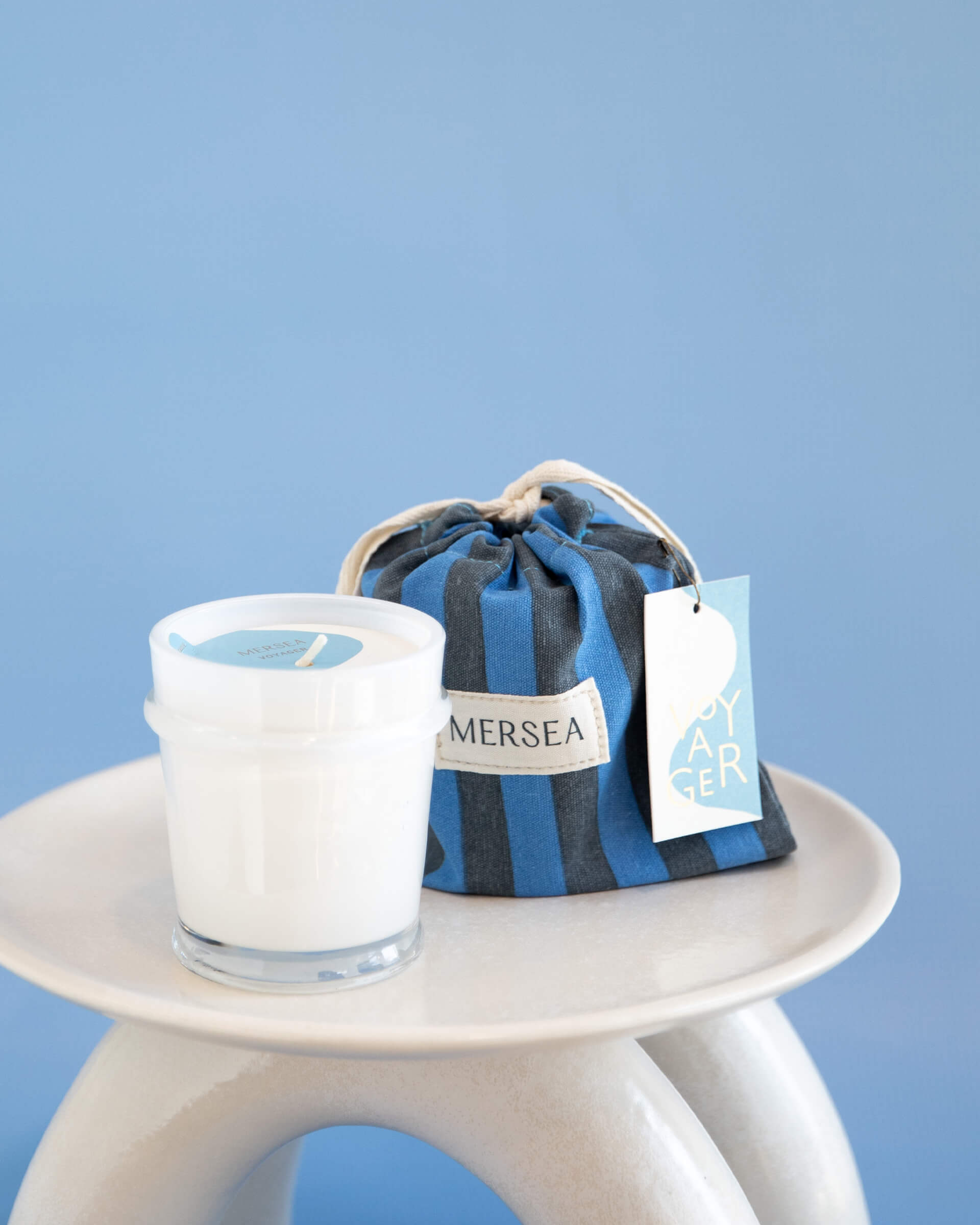 6.5 oz voyager sandbag candle in blue and navy striped bag on a blue background