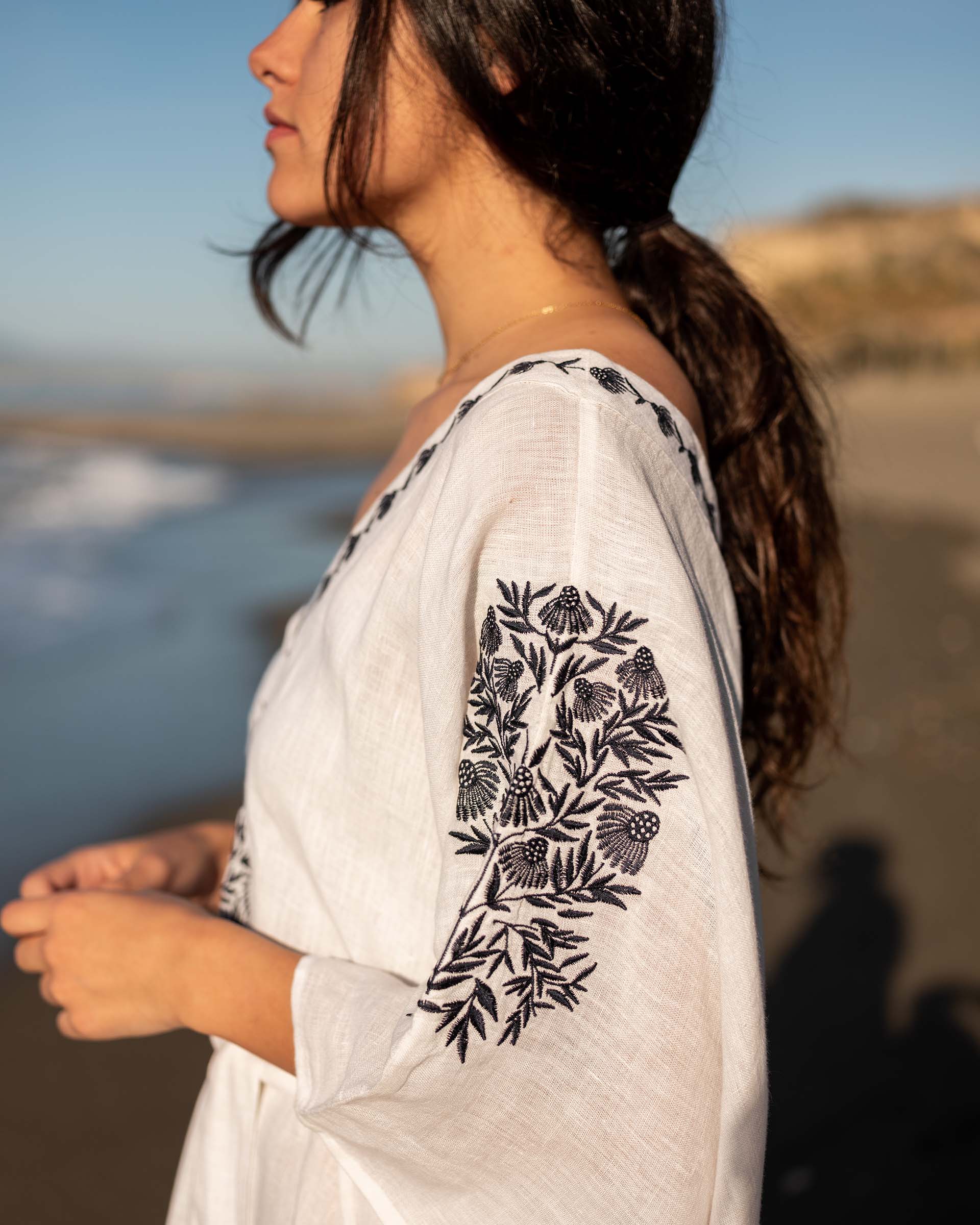 Brown hair female wearing a white embroidered cover up on the beach
