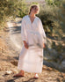 Female wearing a white dress stands in front of olive trees