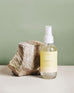 4 oz clear glass bottle of summer day room spray next to a rock on a deep green background