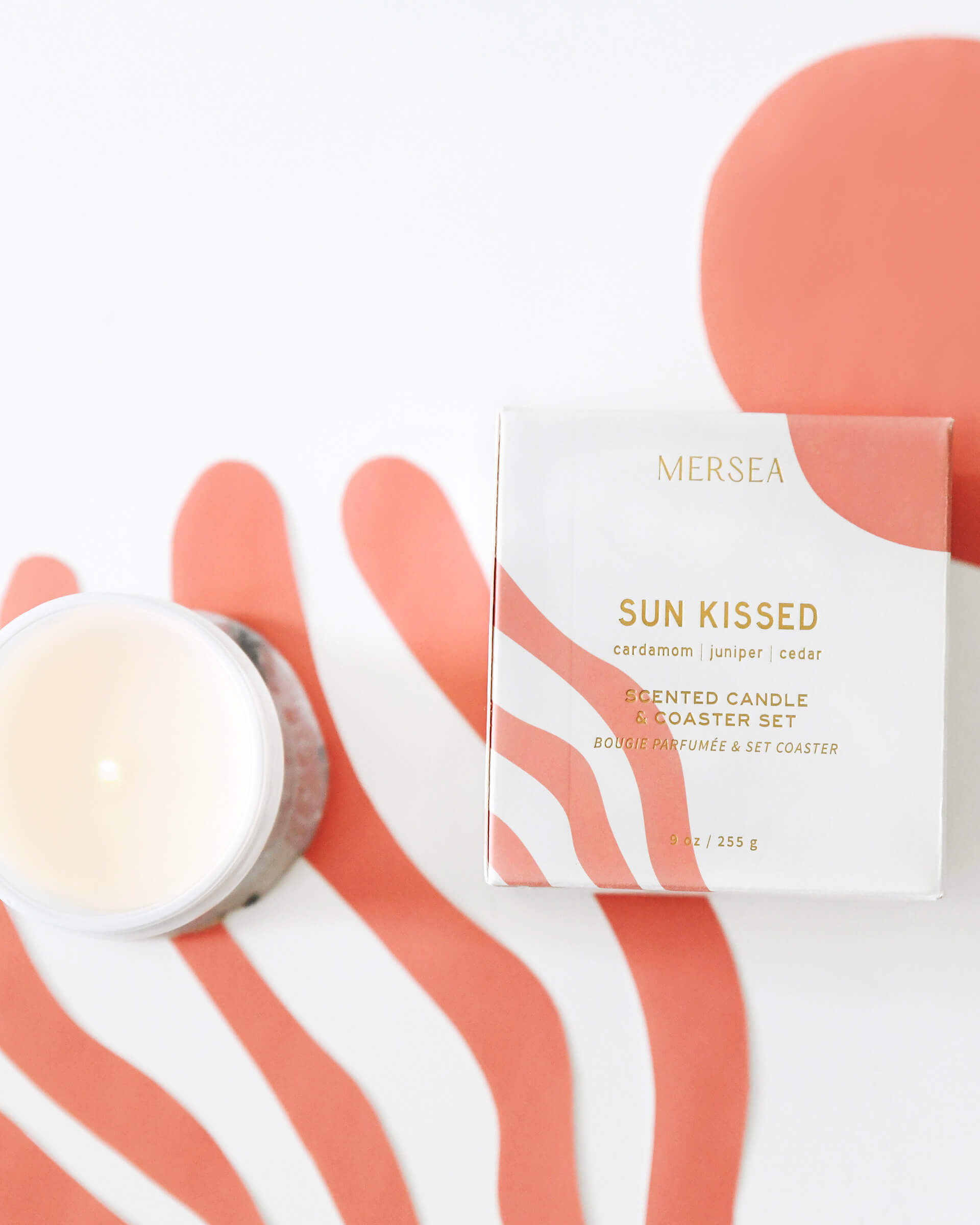 boxed sun kissed candle with coaster and unboxed white candle on coral and white background