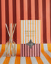 Sun Kissed reed diffuser boxed in orange, red and white stripes on the same striped background 