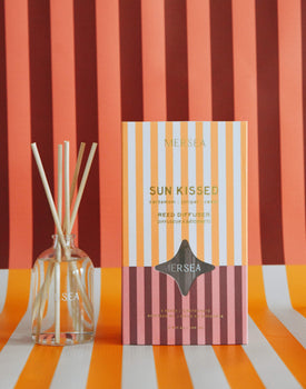 Sun Kissed reed diffuser boxed in orange, red and white stripes on the same striped background 