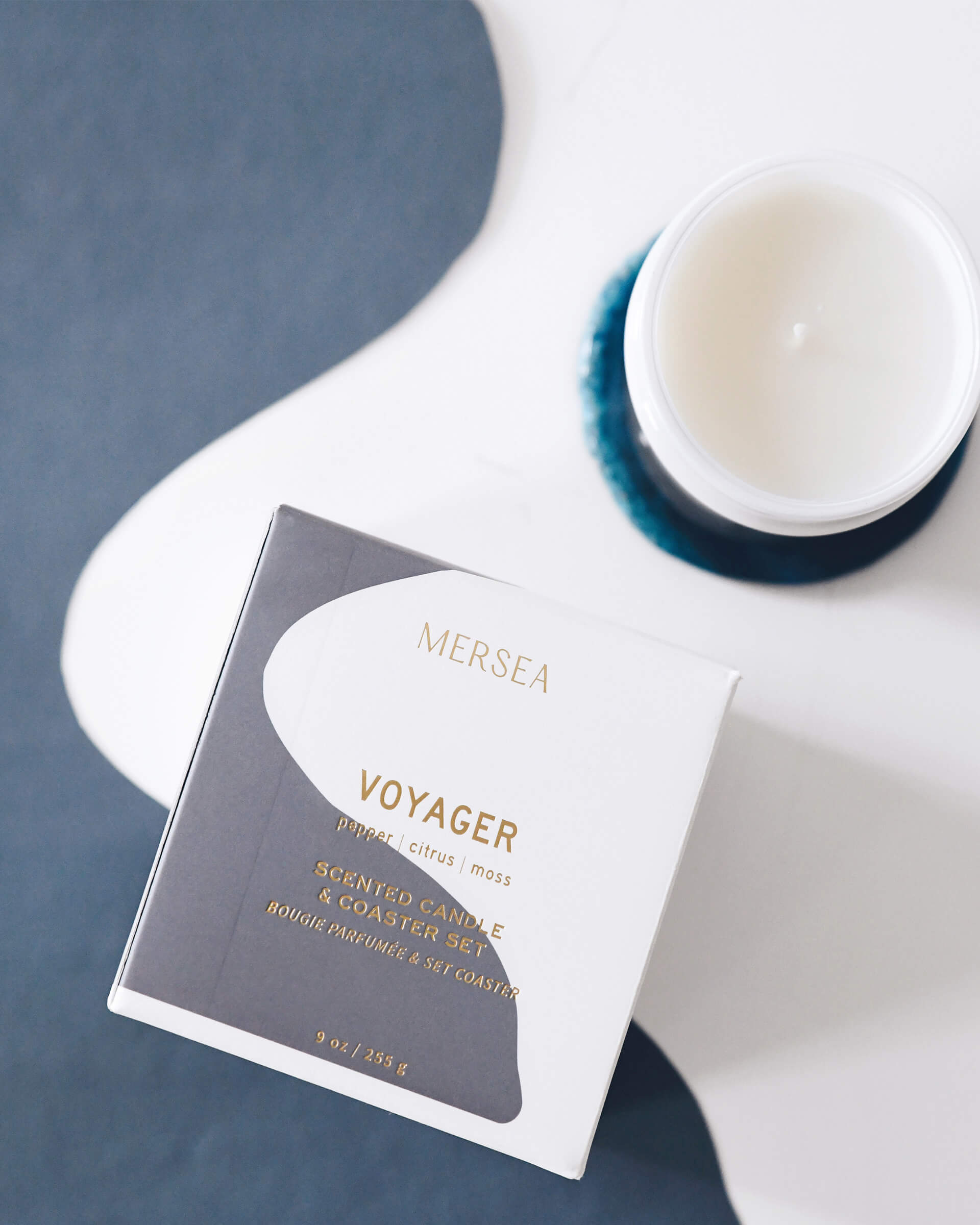 large 9 oz boxed and white voyager candle sitting on blue coaster on white and grey background